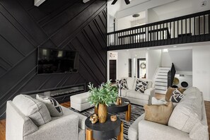A modern living room with a fireplace, a flat-screen TV, and a staircase leading to an upper level.