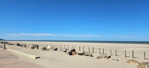 Une plage avec une clôture en bois et des rochers, un ciel dégagé et l’océan en arrière-plan.