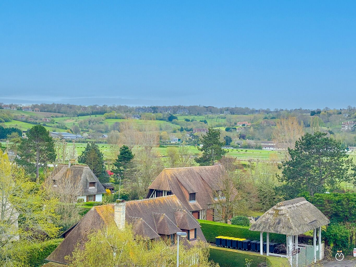 A rural landscape with traditional houses, a thatched structure, and a view of the sea.