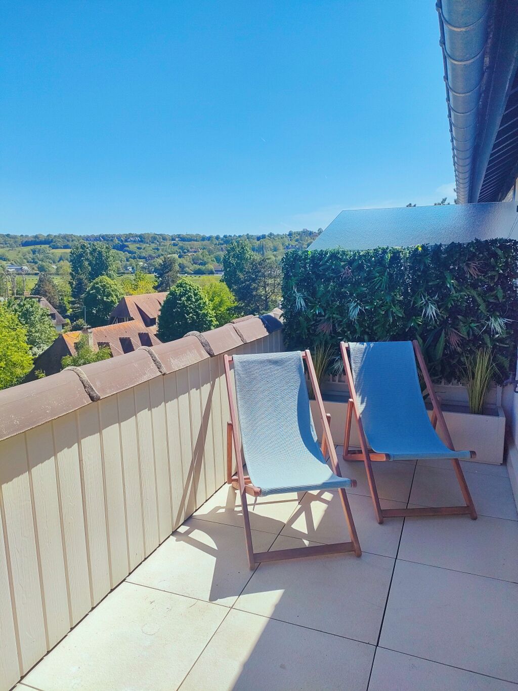 A balcony with two blue lounge chairs, a tiled floor, and a view of a green landscape.