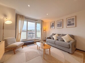 Ein Wohnzimmer mit Sofa, Sessel, Couchtisch und Blick durch ein großes Fenster.