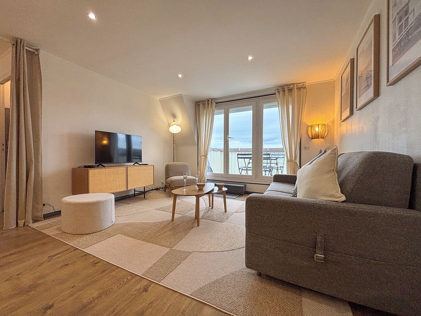 A modern living room with a sofa, a television, a small table, and a balcony with a view.