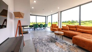 A modern living room with a large sofa, a dining table with chairs, and a view of the outdoors. - Villa Aurora mit Sauna und Whirlpool (Dranske)