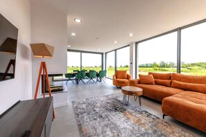 A modern living room with a large sofa, a dining table with chairs, and a view of the outdoors. - Villa Aurora mit Sauna und Whirlpool (Dranske)