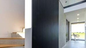 A modern interior with a staircase, a dark vertical panel, and a view of a green field through a glass door. - Villa Aurora mit Sauna und Whirlpool (Dranske)