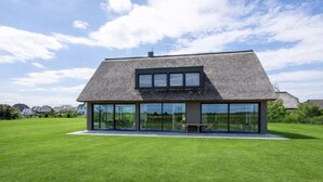 A modern house with a large glass facade, a thatched roof, and a spacious lawn. - Villa Aurora mit Sauna und Whirlpool (Dranske)