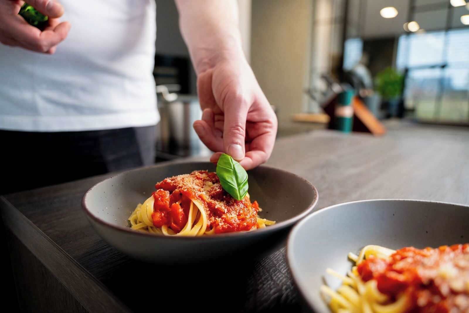 A person placing a basil leaf on a bowl of spaghetti with tomato sauce.