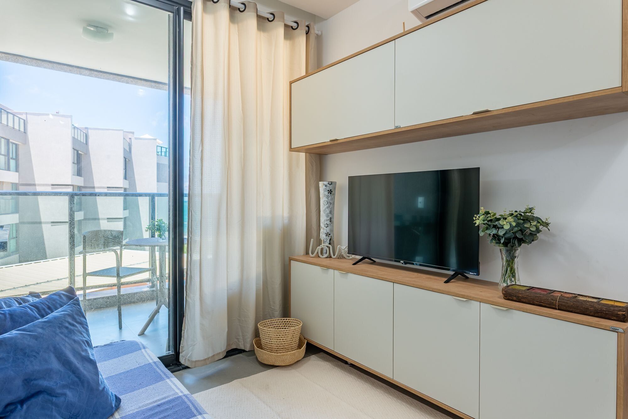 Una sala de estar moderna con un televisor grande, un sofá, una mesita y vistas al exterior.