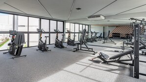 A modern gym with various exercise equipment, large windows, and a clean, spacious layout. - FlatCarneiros-Varanda com Vista-SH152 (Tamandaré)