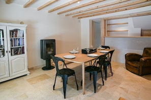 A dining area with a wooden table, four chairs, a cabinet with books, and a television.