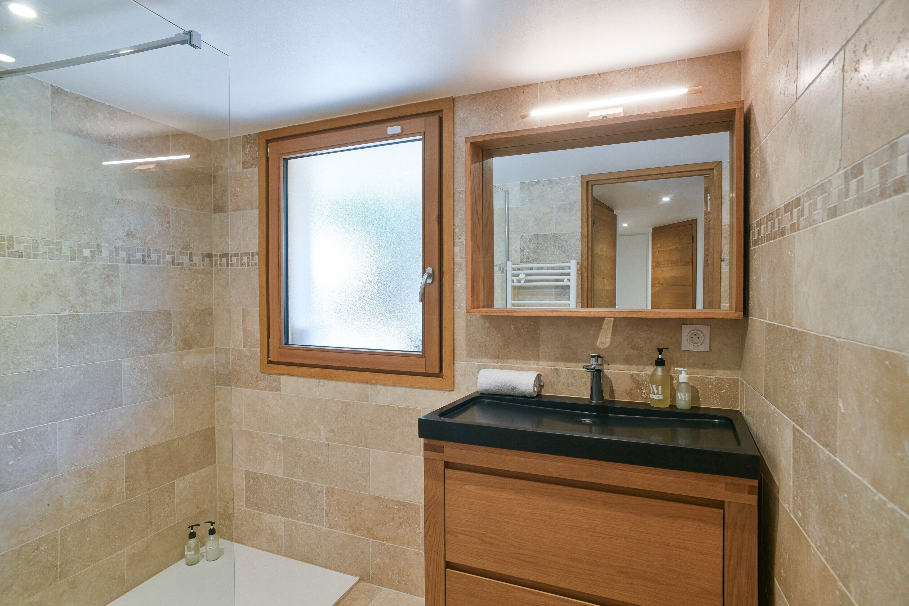 Un baño con cabina de ducha de vidrio, tocador de madera con encimera negra y espejo sobre el tocador.