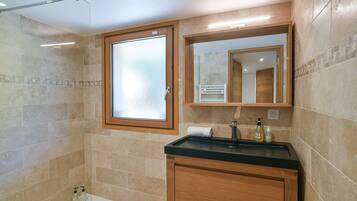 Un baño con cabina de ducha de vidrio, tocador de madera con encimera negra y espejo sobre el tocador.