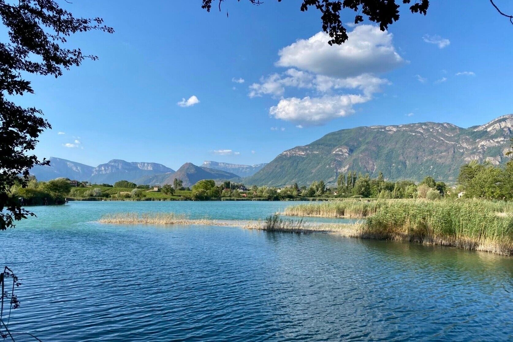 Un lac paisible, avec des montagnes en arrière-plan, entouré de verdure.