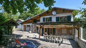 A two-story building with a stone patio, outdoor seating, and a wooden pergola. - Spacious House with Garden & Gym – Porte de Savoie (Porte-de-Savoie)