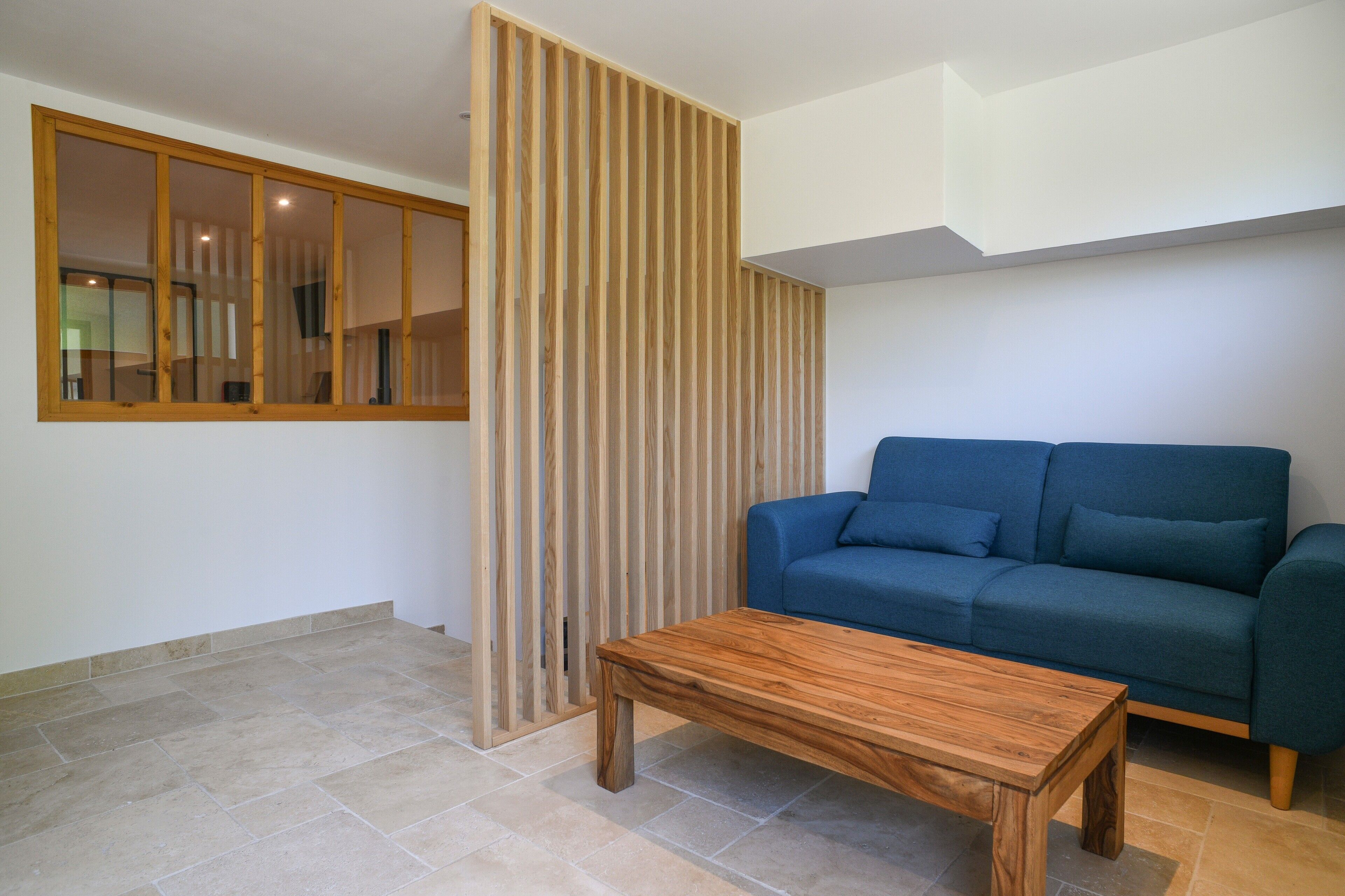 A modern living room with a wooden partition, a blue sofa, and a wooden coffee table.