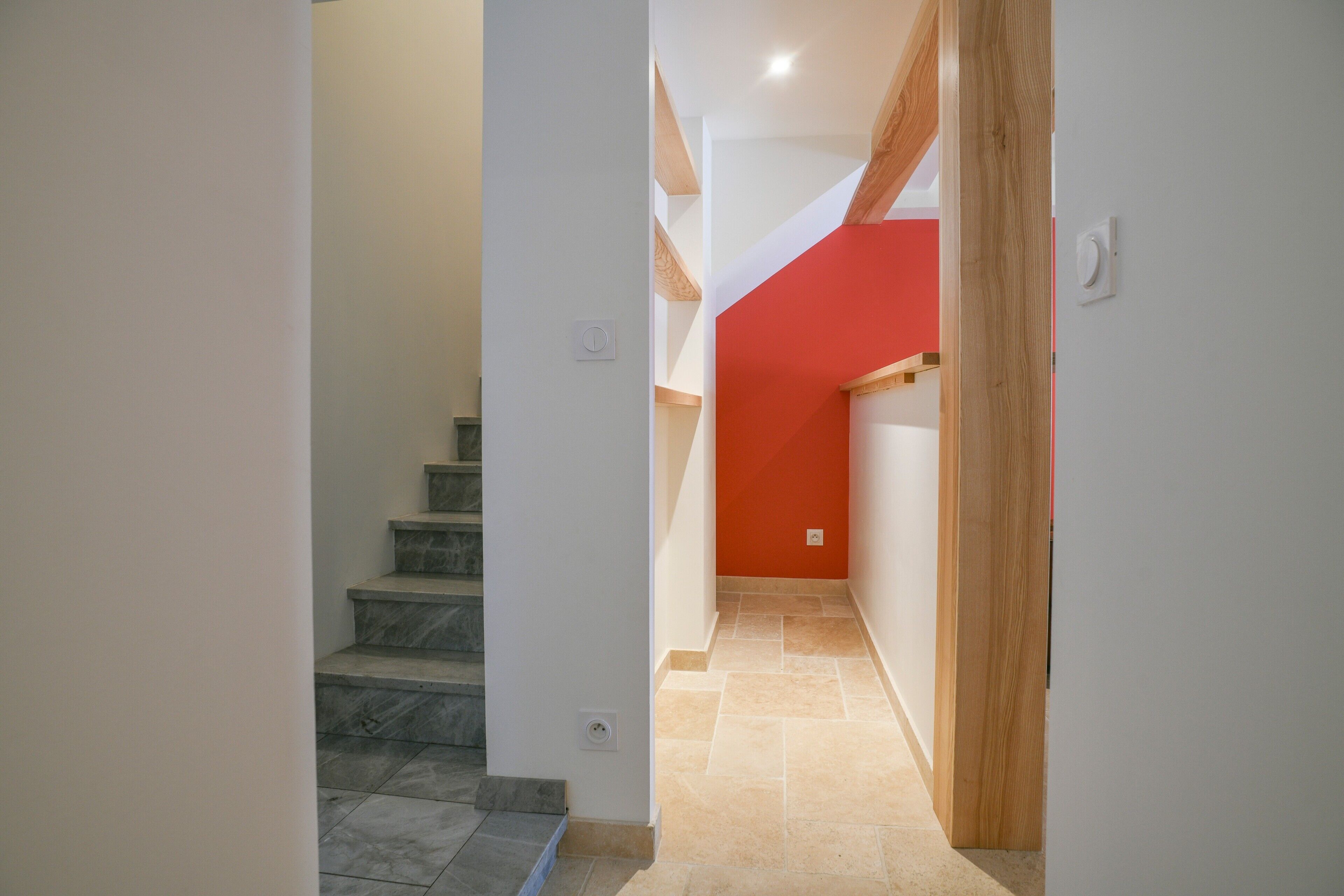 Un escalier menant à une pièce dont un mur est peint en rouge et qui possède un cadre de porte en bois.