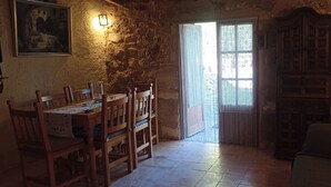 Una habitación rústica con pared de piedra, una mesa de madera con sillas, una estantería y una cortina estampada.
