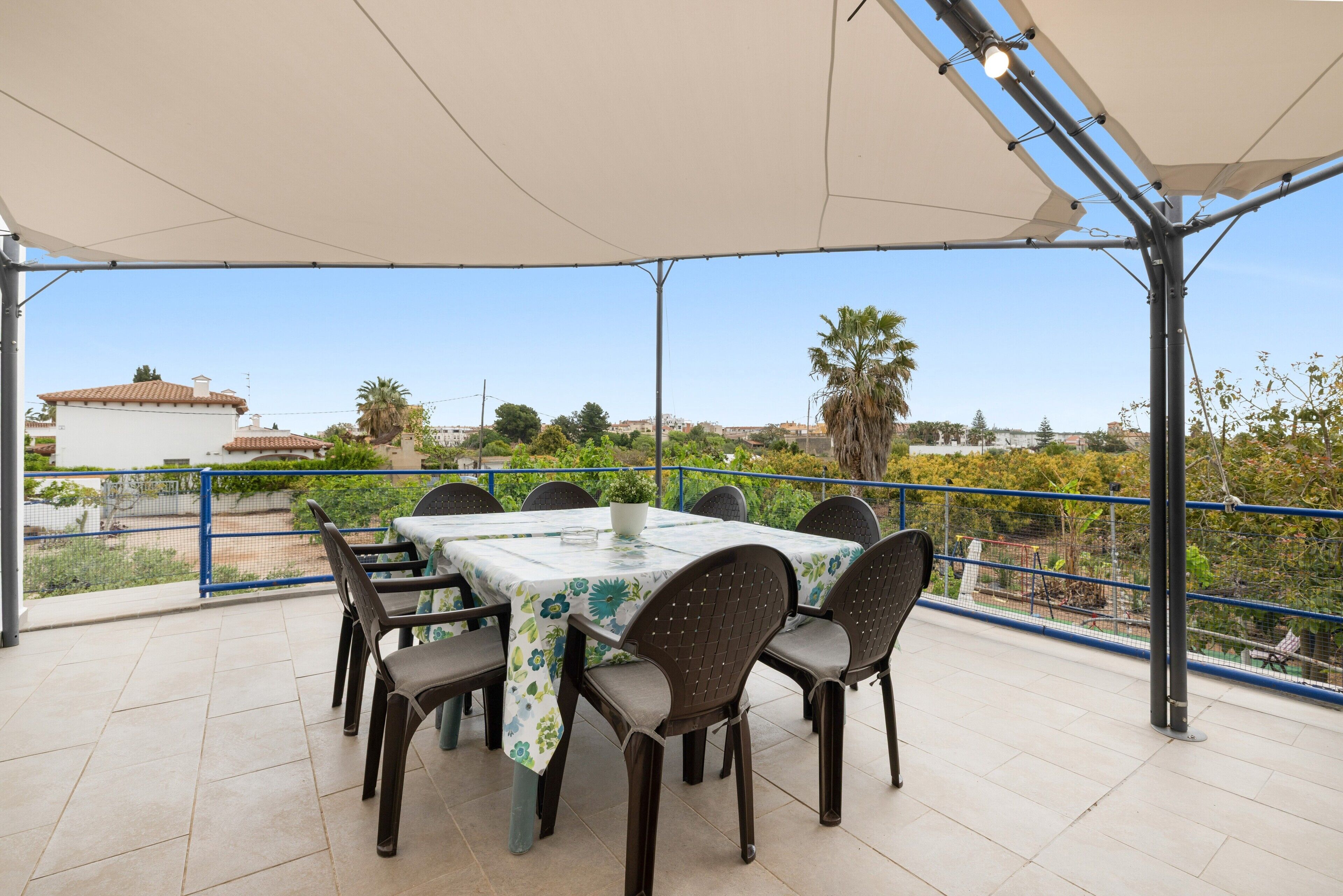 Un patio techado al aire libre con una mesa y sillas, vistas del entorno y una barandilla.
