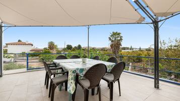 Un patio techado al aire libre con una mesa y sillas, vistas del entorno y una barandilla.