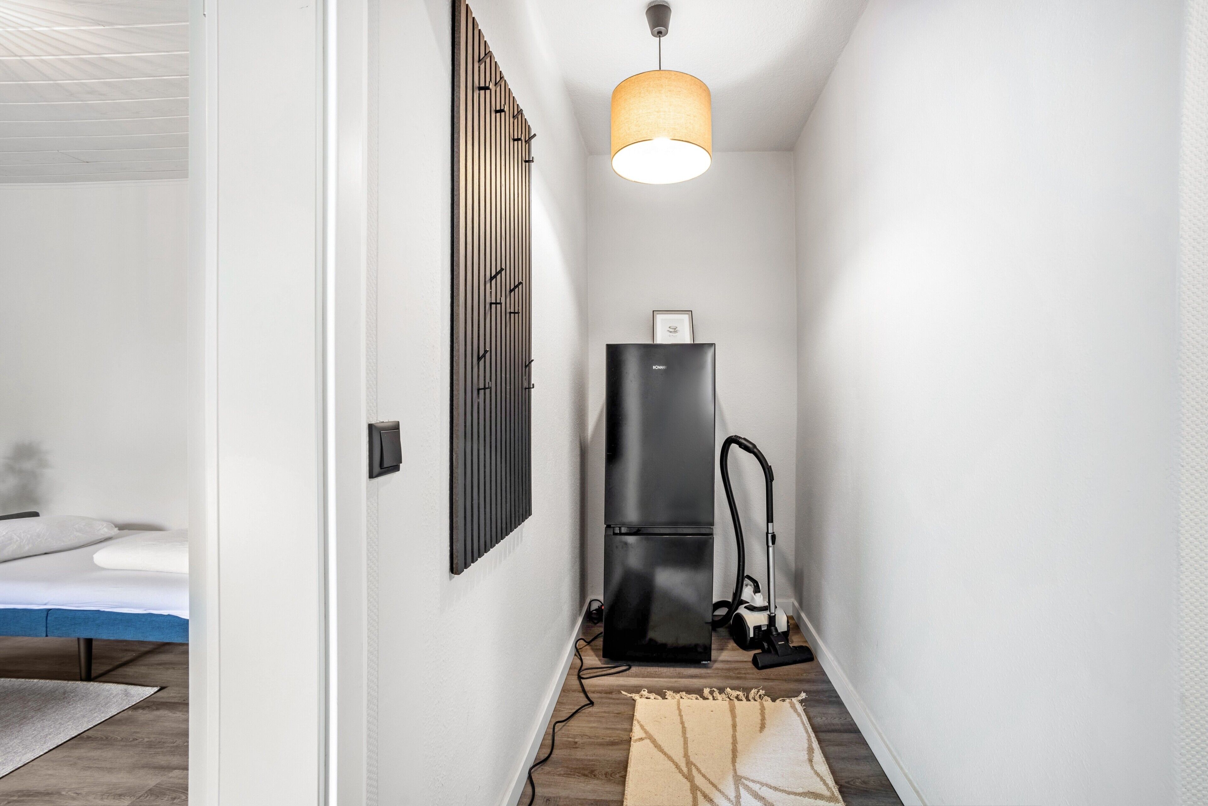 A narrow hallway with a black refrigerator, a vacuum cleaner, and a hanging light fixture.