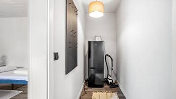 A narrow hallway with a black refrigerator, a vacuum cleaner, and a hanging light fixture.