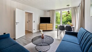 A modern living room with a sofa, a coffee table, a TV, and a dining area with chairs.