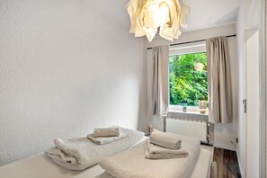 A room with two beds, a window with curtains, a radiator, and a hanging light fixture. - Apartment Kleine Seeperle in Quickborn – Quiet, Modern, and Well Connected (Quickborn)