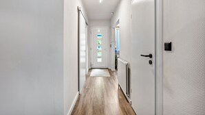 A narrow hallway with a wooden floor, white walls, and a door at the end.