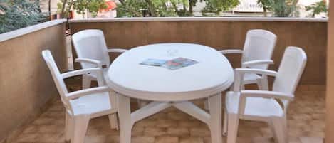 Una mesa redonda blanca con cuatro sillas blancas en un patio empedrado.