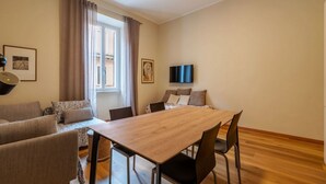 Ein Zimmer mit einem Holzespeisetisch, vier Stühlen, einer Couch, einem Fernseher und einem Fenster mit Vorhängen.