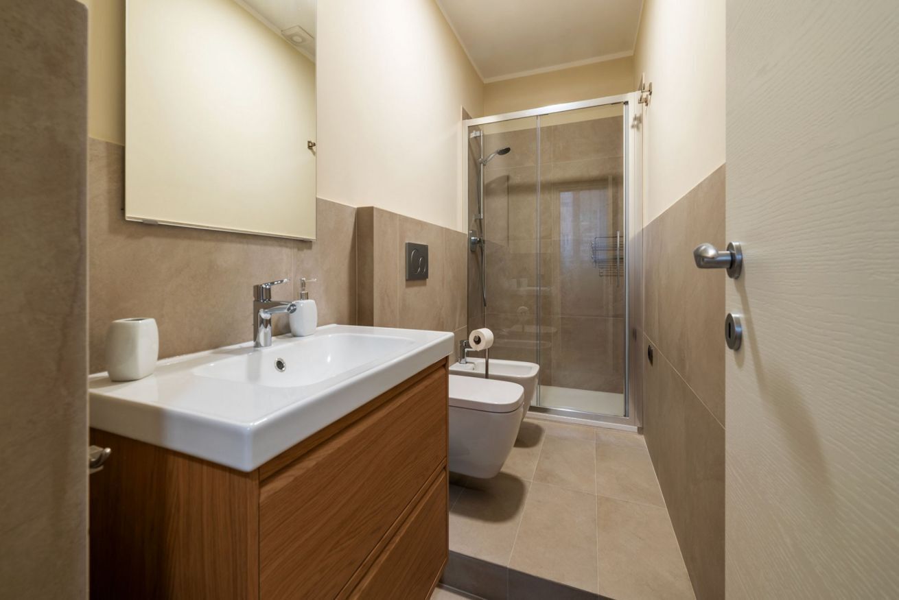 A modern bathroom with a double sink, a toilet, and a glass shower enclosure.