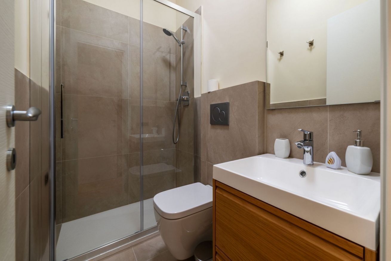 A bathroom with a glass shower enclosure, a white toilet, a wooden vanity with a white sink, and a mirror above the sink.