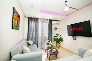 A modern living room with a sofa, a coffee table, a TV, and a potted plant. - Chic Designer Apartment with Pool Access (Agadir)