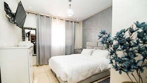 Ein Schlafzimmer mit einem Bett, einem an der Wand montierten Fernseher, einem Nachttisch, einem Spiegel und einer Topfpflanze.