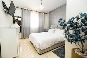 A bedroom with a bed, a TV mounted on the wall, a bedside table, a mirror, and a potted plant. - Chic Designer Apartment with Pool Access (Agadir)