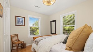 A bedroom with a bed, a chair, two windows with blinds, a ceiling fan, and a framed picture on the wall. - Cozy, Quiet 2 Bedroom with Hot Tub, Fire Pit, Close to Fayetteville (Winslow)