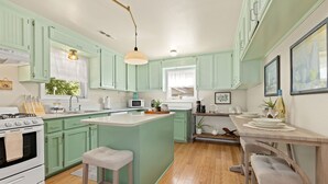A kitchen with green cabinets, a white stove, a central island, and a dining area with a table and chairs. - Cozy, Quiet 2 Bedroom with Hot Tub, Fire Pit, Close to Fayetteville (Winslow)