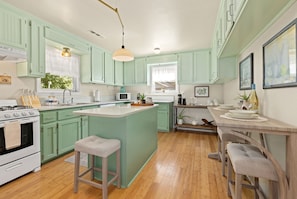A kitchen with green cabinets, a white stove, a central island, and a dining area with a table and chairs.