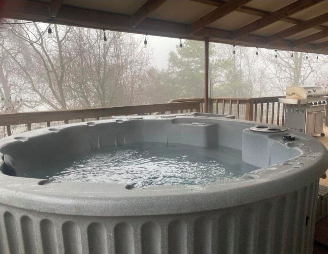 A hot tub with a wooden deck and a grill in the background.