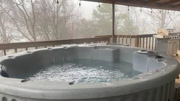 A hot tub with a wooden deck and a grill in the background.