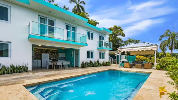 Et moderne hus i to etager med swimmingpool, udendørs møbler og en overdækket terrasse.
