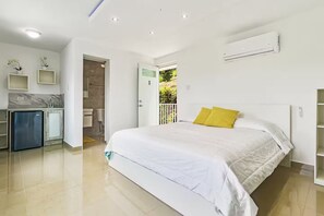 Ein Hotelzimmer mit Bett, einer kleinen Küchenzeile, einem Badezimmer und einem Balkon mit Blick.