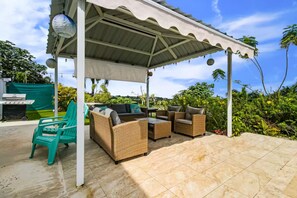 Eine Terrasse im Freien mit Korbmöbeln, einem Grill und einem überdachten Bereich.