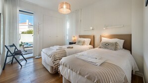 Une chambre d’hôtel avec deux lits, une chaise, une lampe et une vue sur l’extérieur, visible à travers une porte.