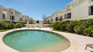 Une piscine avec des chaises longues, un parasol et un bâtiment doté de balcons.