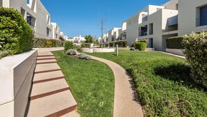 Un immeuble résidentiel moderne doté d’une pelouse bien entretenue, d’un chemin sinueux et surplombé d’un ciel bleu dégagé.