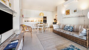 Un salon moderne comprenant un canapé, un téléviseur et un coin repas avec des chaises et une table.