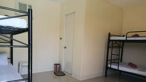 A dormitory room with bunk beds, a door, a trash bin, and a white wall. - Room-1 Person in 6 bed Mixed Dormitory (Puerto Galera)