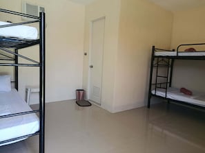 A dormitory room with bunk beds, a door, a trash bin, and a white wall. - Room-1 Person in 6 bed Mixed Dormitory (Puerto Galera)