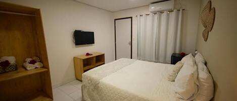 A bedroom with a bed, a wooden wardrobe, a television, and a wall-mounted air conditioner.